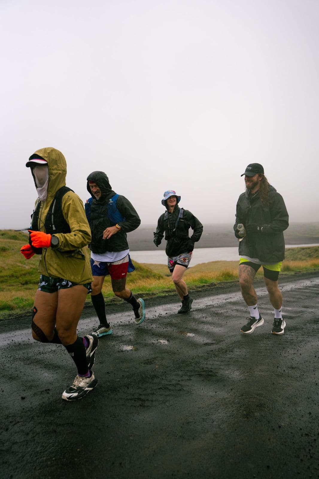 Runners in rain shells pushing through fog on a wet gravel road