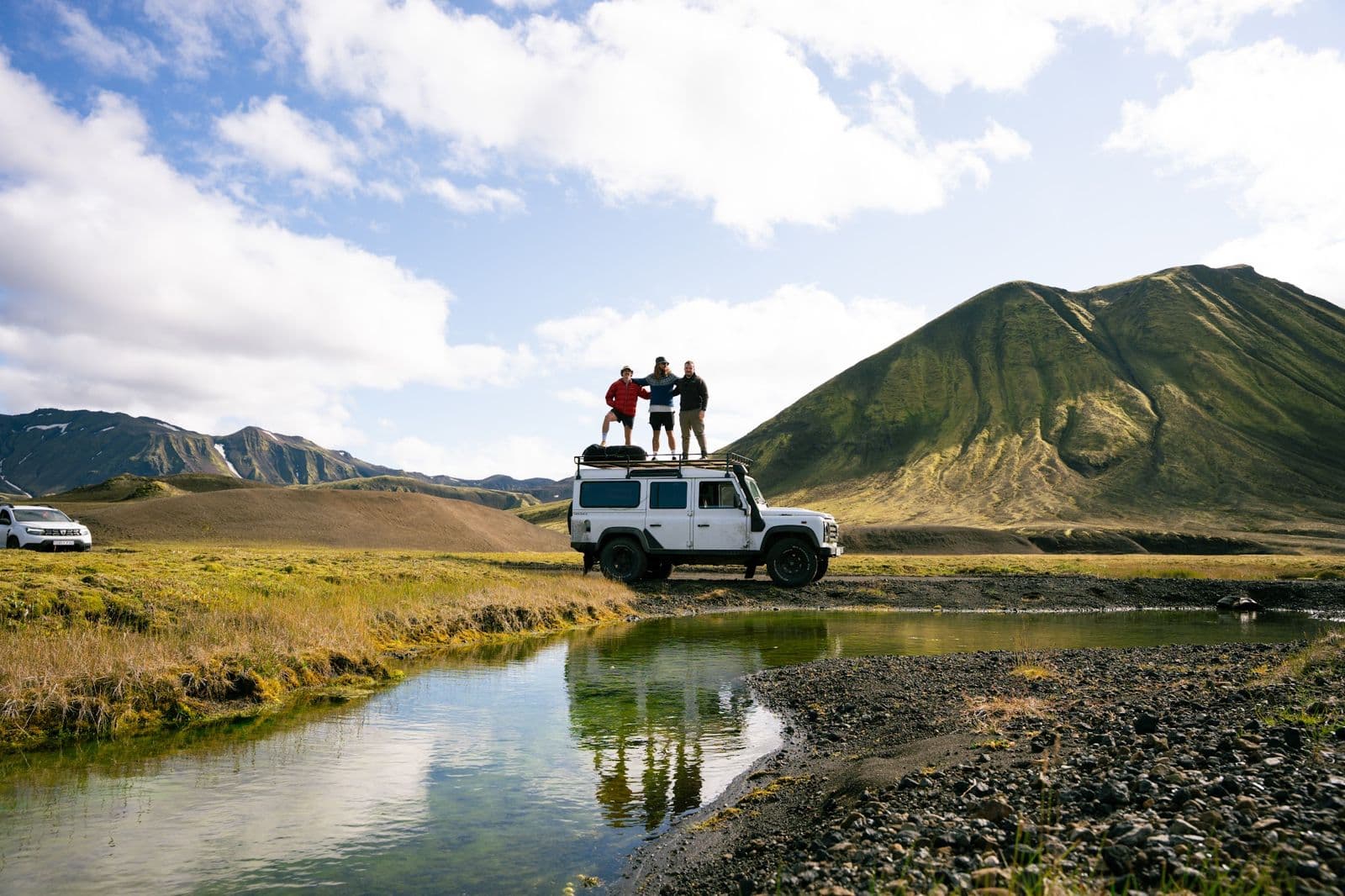 The crew on the roof of the Land Rover, mirrored in a highland river